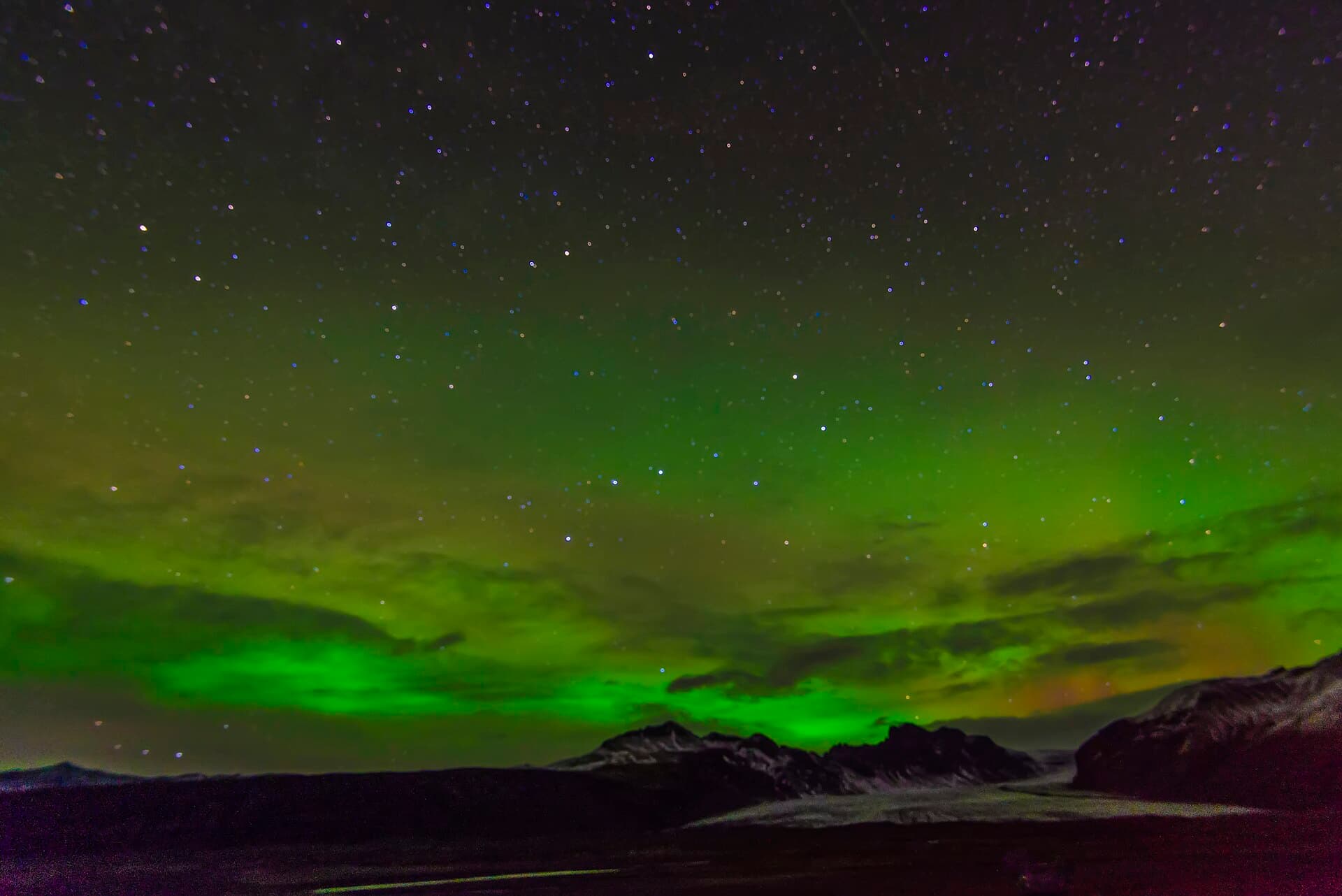 Green bands of the aurora borealis over snow-dusted mountains and a glacier in Iceland