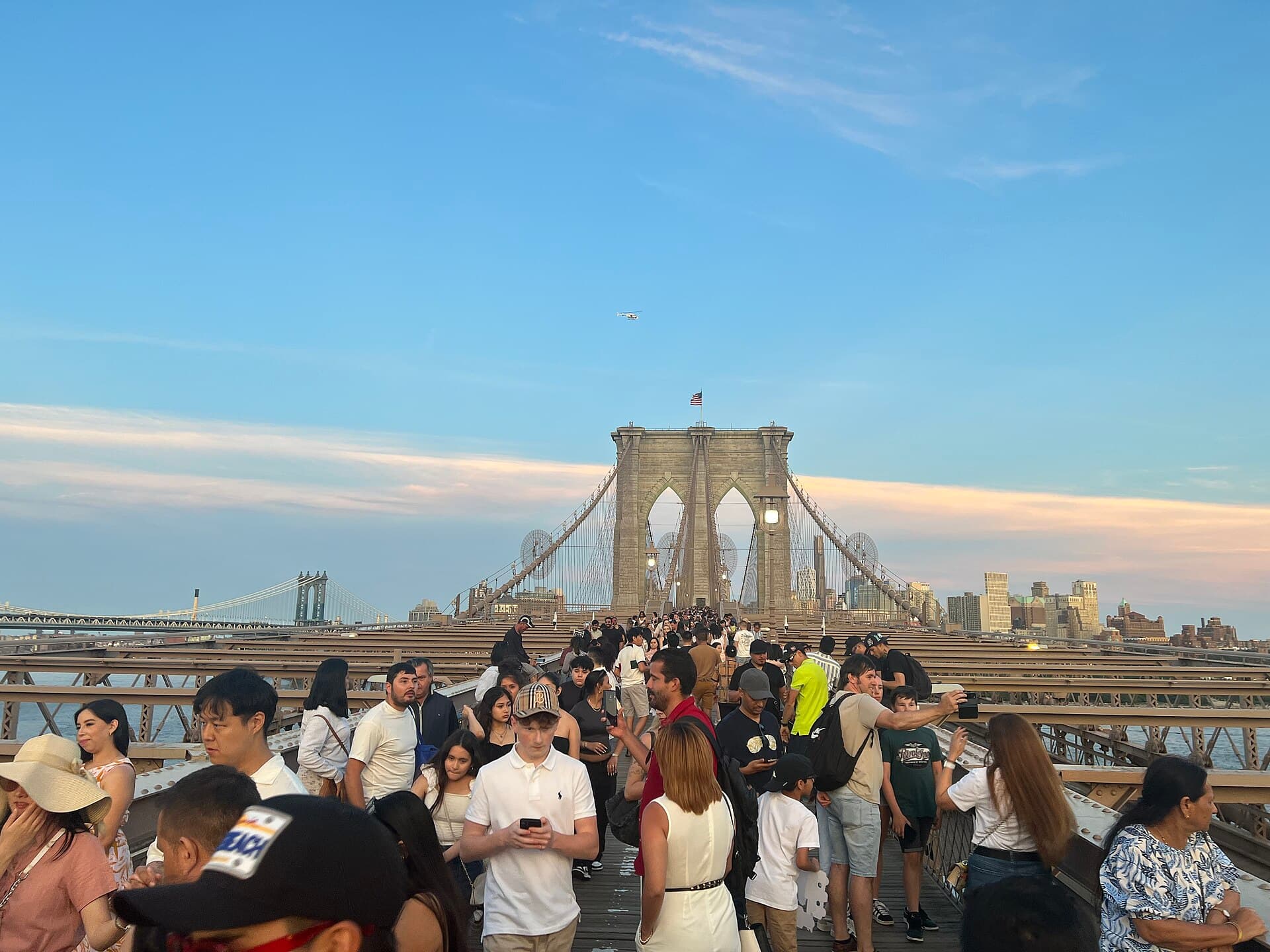 Visitors walking across the Brooklyn Bridge toward its stone tower